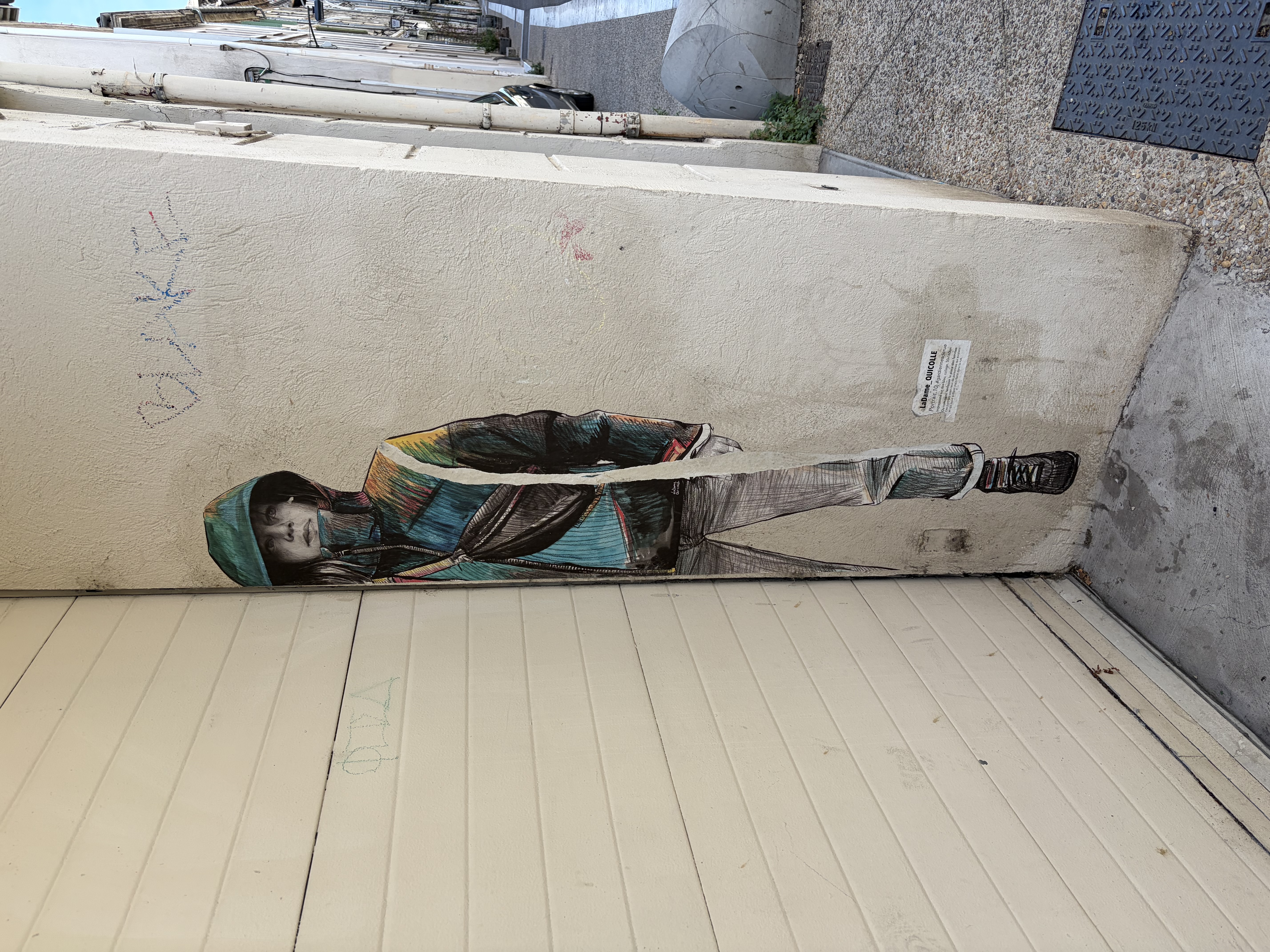 Life sized wall painting of a woman in a grey gown on rough lime plaster, beside it olive branches and a wrought iron sign in an old town lane of Provence