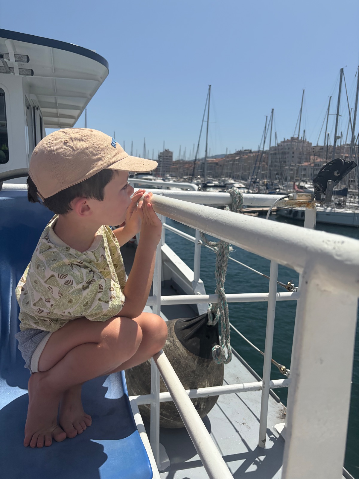 Vier Bilder aus einer Tagestour: Ein Kind sitzt auf der Reling eines Bootes mit Mütze und schaut auf einen Hafen voller Segelschiffe; kristallklares Wasser an einer felsigen Küste mit alten Befestigungsanlagen; ein Leuchtturm auf einer Felsinsel in klarem Wasser.