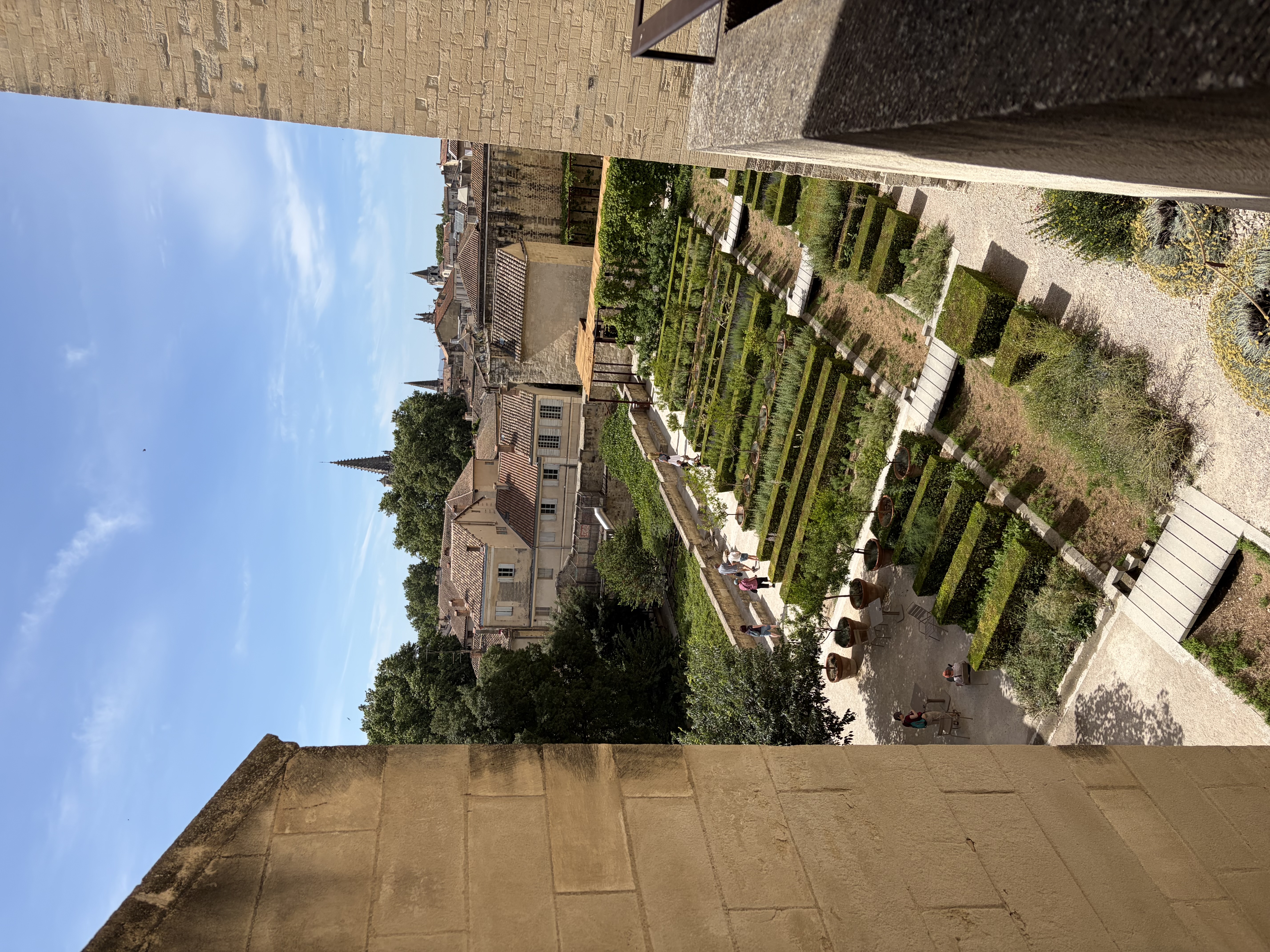 Helles Steingebäude mit regelmäßigen Fensteröffnungen, überwachsen mit grünem Efeu, akkurat angelegter Garten mit strukturierten Hecken und einzelnen Blüten davor, lange Galerie mit Säulen und hohen Räumen, mediterrane Gartenarchitektur in Marseille